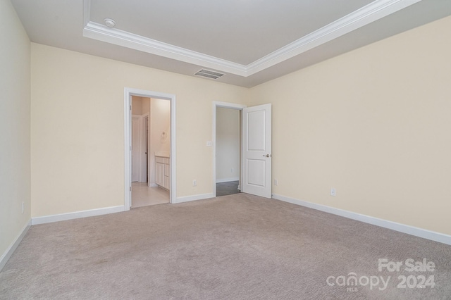 unfurnished bedroom featuring ornamental molding, light colored carpet, a raised ceiling, and ensuite bath