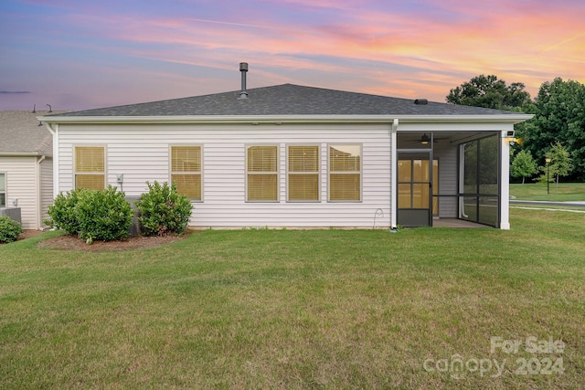 back house at dusk featuring a sunroom and a yard