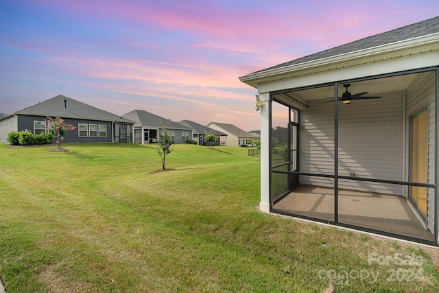 yard at dusk featuring ceiling fan and a sunroom