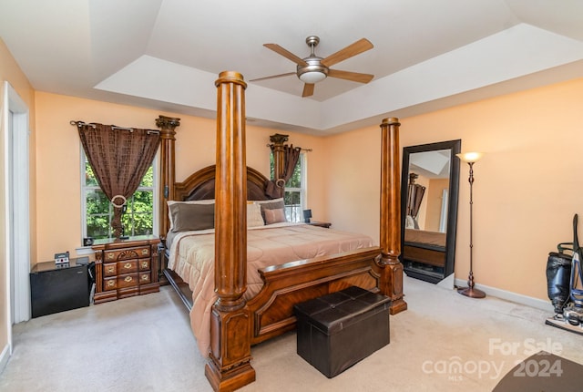 bedroom with ceiling fan, light colored carpet, decorative columns, and a raised ceiling