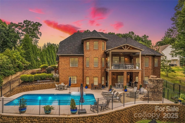 back house at dusk with a fenced in pool, a patio area, and a balcony