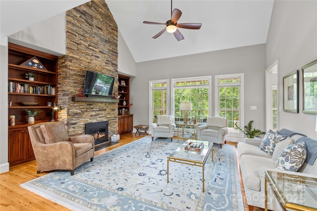 living room with ceiling fan, a stone fireplace, light hardwood / wood-style floors, and high vaulted ceiling