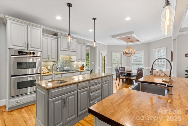 kitchen featuring gray cabinets, an island with sink, sink, and stainless steel appliances