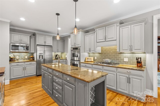 kitchen featuring gray cabinetry, light stone counters, hanging light fixtures, stainless steel appliances, and a kitchen island with sink