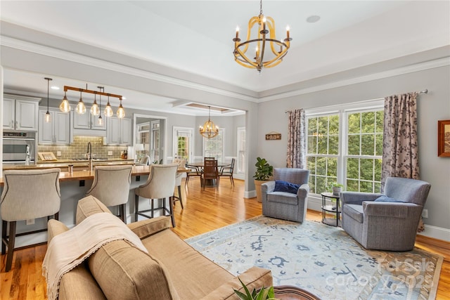 living room featuring crown molding, sink, a chandelier, and light hardwood / wood-style flooring