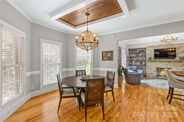 dining space with a raised ceiling, a stone fireplace, a chandelier, and light hardwood / wood-style floors