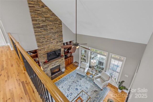 living room with hardwood / wood-style flooring, ceiling fan, a stone fireplace, and high vaulted ceiling