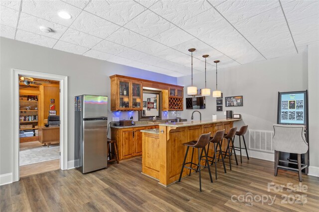 kitchen featuring a breakfast bar area, hanging light fixtures, stainless steel refrigerator, dark hardwood / wood-style floors, and kitchen peninsula