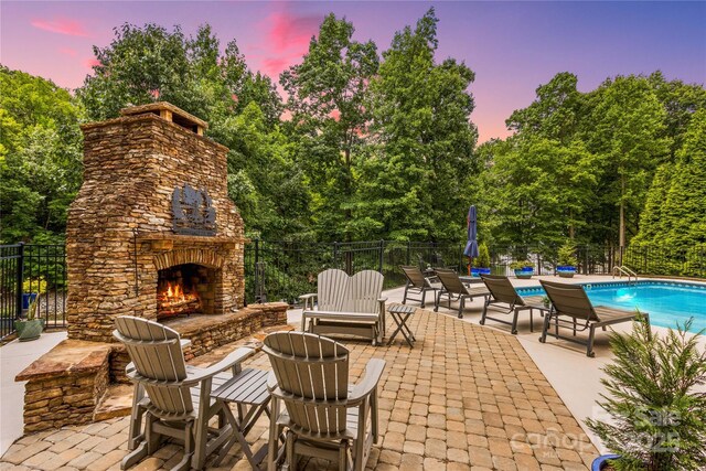 patio terrace at dusk featuring a fenced in pool and an outdoor stone fireplace