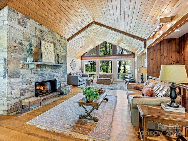 living room with light hardwood / wood-style floors, a stone fireplace, and wood ceiling