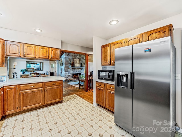 kitchen featuring kitchen peninsula, stainless steel fridge with ice dispenser, and a stone fireplace