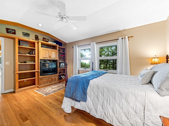 bedroom featuring a textured ceiling, light hardwood / wood-style flooring, vaulted ceiling, and ceiling fan