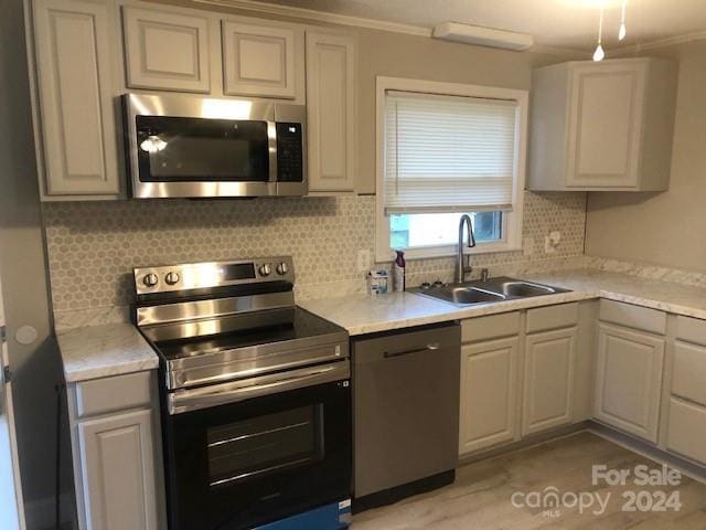 kitchen featuring backsplash, sink, crown molding, appliances with stainless steel finishes, and light tile patterned floors