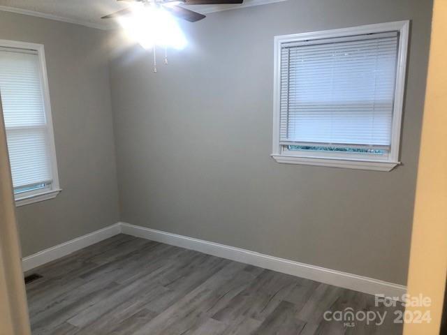 empty room featuring dark wood-type flooring, crown molding, and ceiling fan