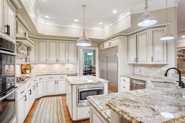 kitchen with built in appliances, light stone countertops, pendant lighting, a kitchen island, and sink