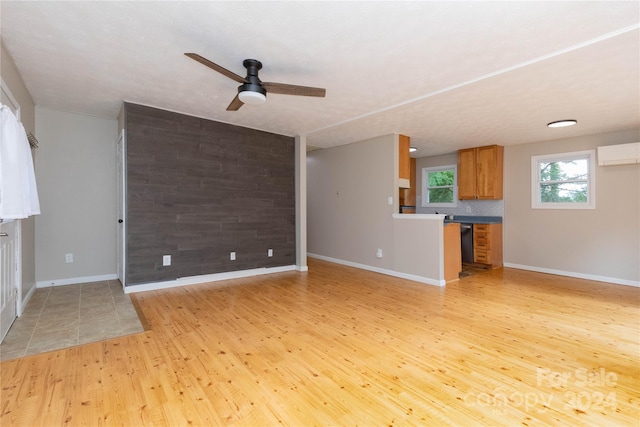 unfurnished living room featuring ceiling fan, an AC wall unit, light hardwood / wood-style floors, and wood walls