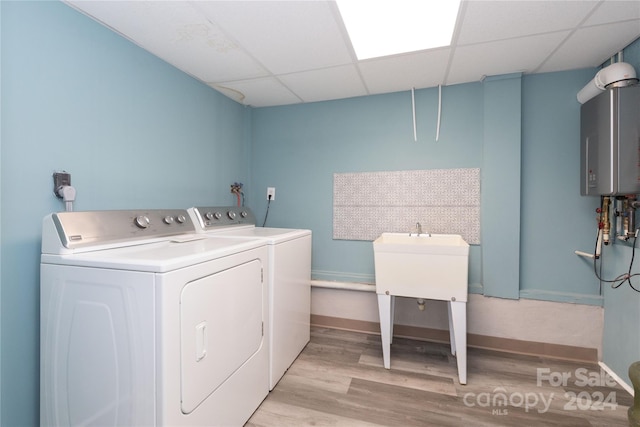 washroom with washing machine and clothes dryer, baseboards, water heater, and light wood-style floors