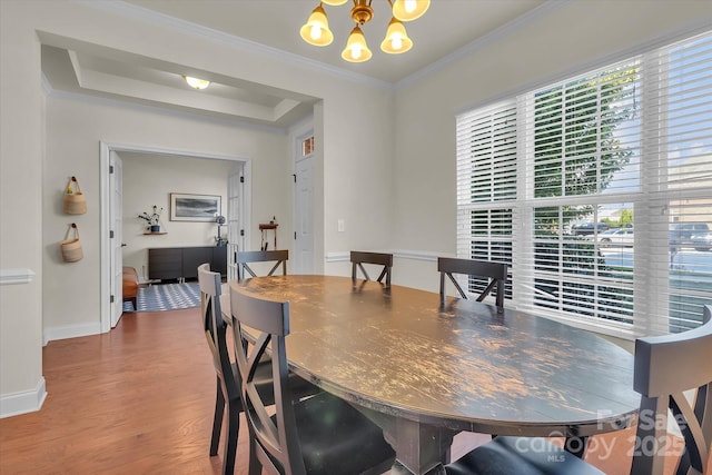 dining area featuring a notable chandelier, wood-type flooring, ornamental molding, and a tray ceiling