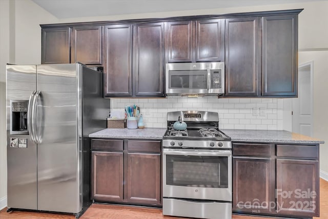 kitchen with dark brown cabinets, light stone counters, appliances with stainless steel finishes, and tasteful backsplash