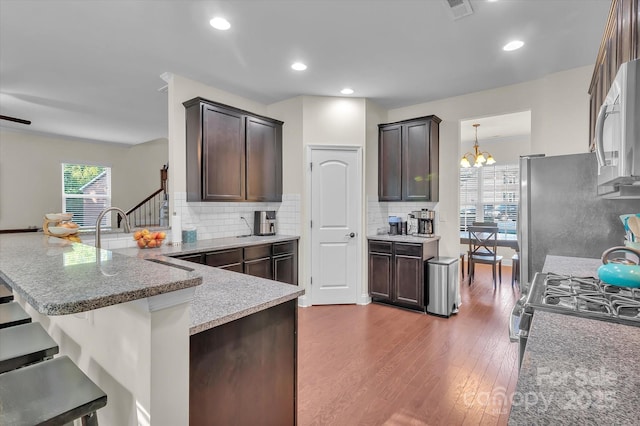 kitchen featuring a breakfast bar, dark wood-type flooring, an inviting chandelier, appliances with stainless steel finishes, and dark brown cabinetry