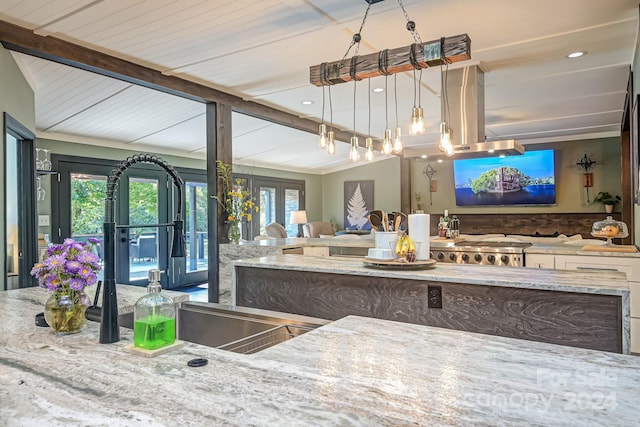 kitchen with decorative light fixtures, light stone counters, lofted ceiling with beams, and french doors