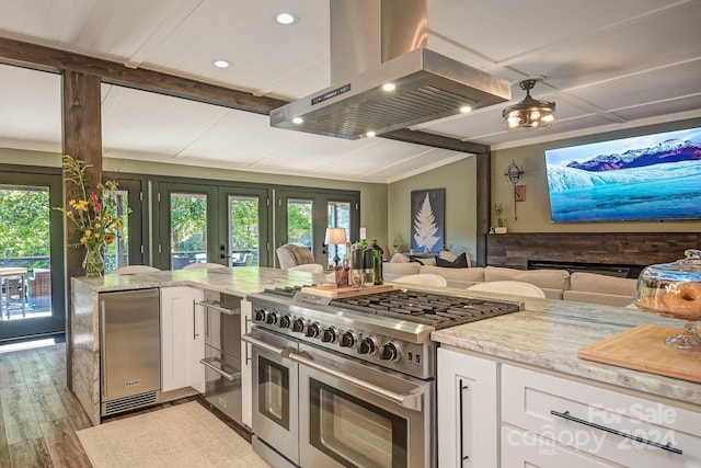 kitchen featuring white cabinets, island exhaust hood, double oven range, refrigerator, and light stone counters