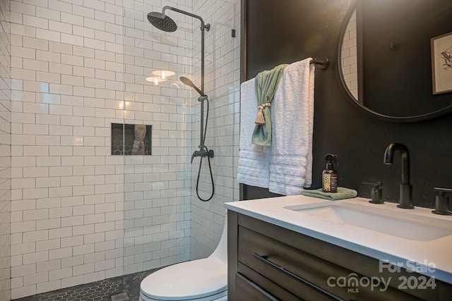 bathroom with toilet, a tile shower, and vanity