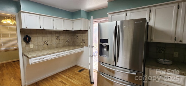 kitchen with tasteful backsplash, light hardwood / wood-style flooring, tile counters, stainless steel fridge, and white cabinets