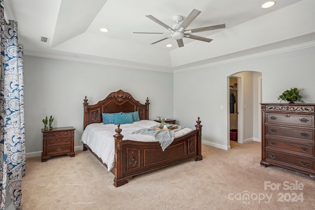 carpeted bedroom featuring a raised ceiling, a walk in closet, ceiling fan, and ornamental molding