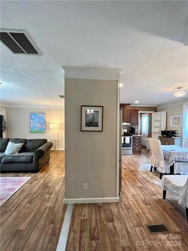 hall with wood-type flooring, ornamental molding, and a textured ceiling