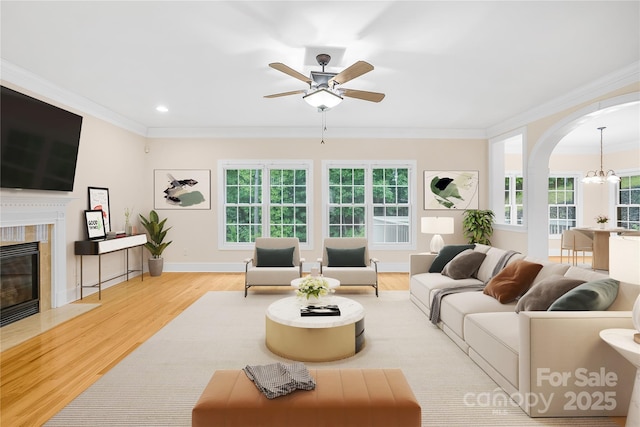 living room featuring light hardwood / wood-style floors, a high end fireplace, crown molding, and ceiling fan with notable chandelier