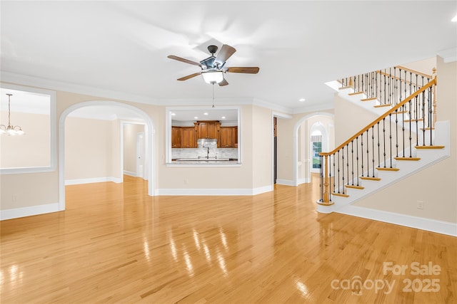 unfurnished living room featuring crown molding, ceiling fan with notable chandelier, and light hardwood / wood-style floors