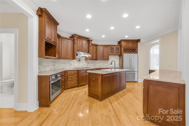 kitchen featuring an island with sink, stainless steel appliances, light wood-type flooring, ornamental molding, and sink