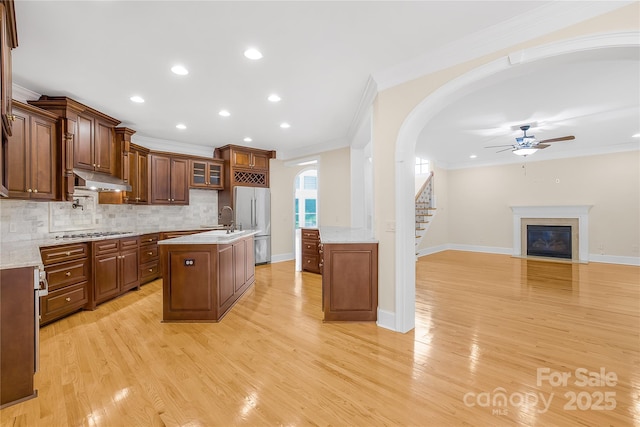 kitchen featuring light hardwood / wood-style floors, decorative backsplash, crown molding, appliances with stainless steel finishes, and an island with sink