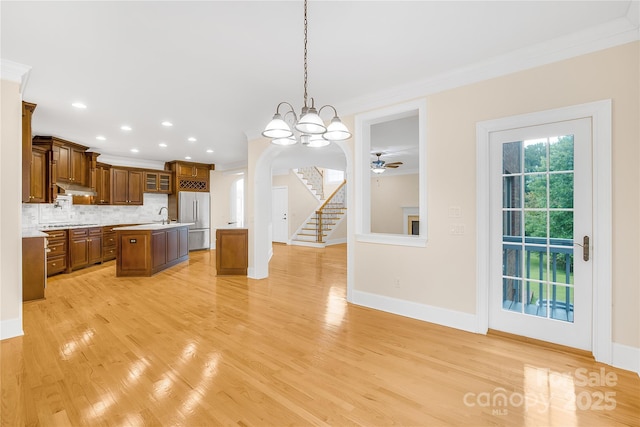 kitchen with built in refrigerator, a center island, backsplash, hanging light fixtures, and crown molding