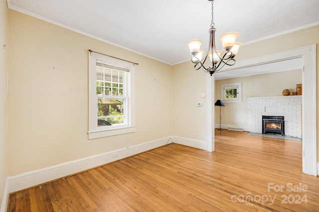 unfurnished living room featuring crown molding, a brick fireplace, light hardwood / wood-style flooring, and a notable chandelier