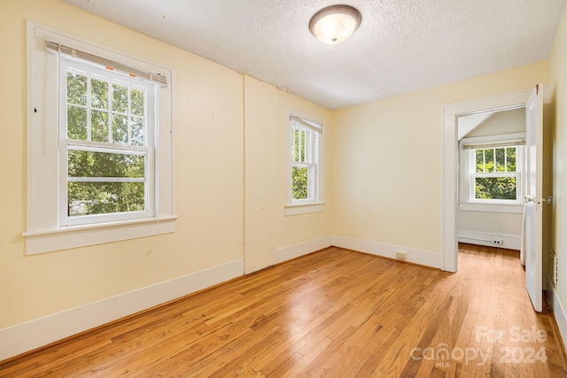 spare room with plenty of natural light, a textured ceiling, and light hardwood / wood-style floors