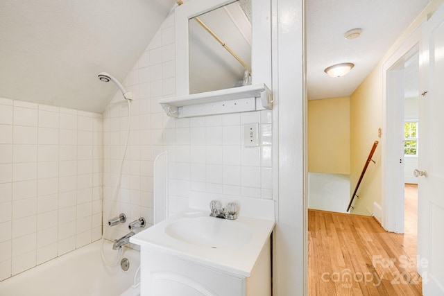 bathroom with tiled shower / bath combo, hardwood / wood-style floors, vaulted ceiling, and vanity