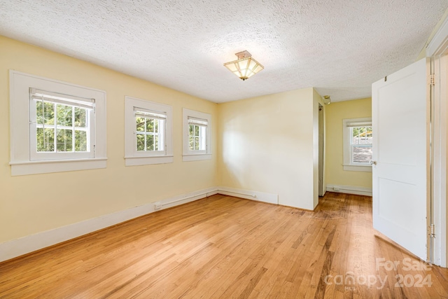 empty room with a textured ceiling, light hardwood / wood-style flooring, and a healthy amount of sunlight