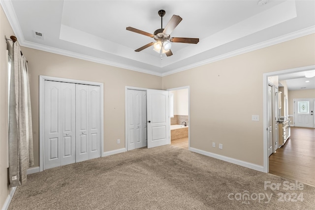 unfurnished bedroom with ornamental molding, carpet flooring, ceiling fan, a tray ceiling, and multiple closets