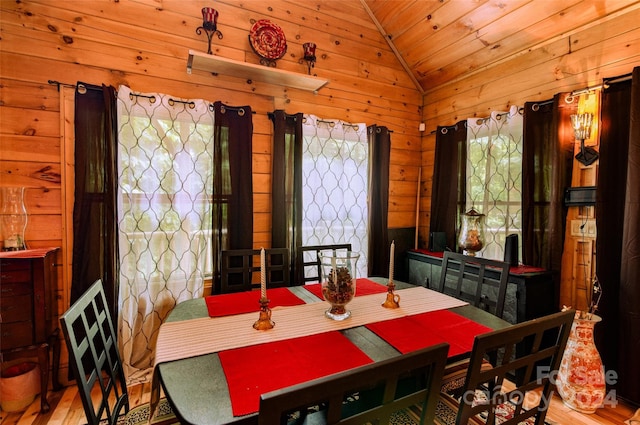 dining room featuring light wood-type flooring, wooden walls, and vaulted ceiling