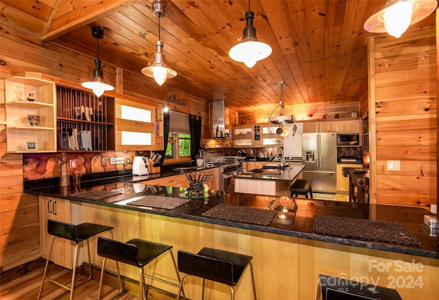 kitchen featuring decorative light fixtures, kitchen peninsula, stainless steel fridge, and wood walls