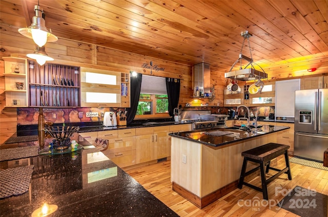 kitchen with a breakfast bar, pendant lighting, stainless steel fridge with ice dispenser, and an island with sink