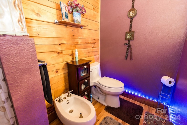 bathroom featuring a bidet, toilet, hardwood / wood-style floors, and wood walls