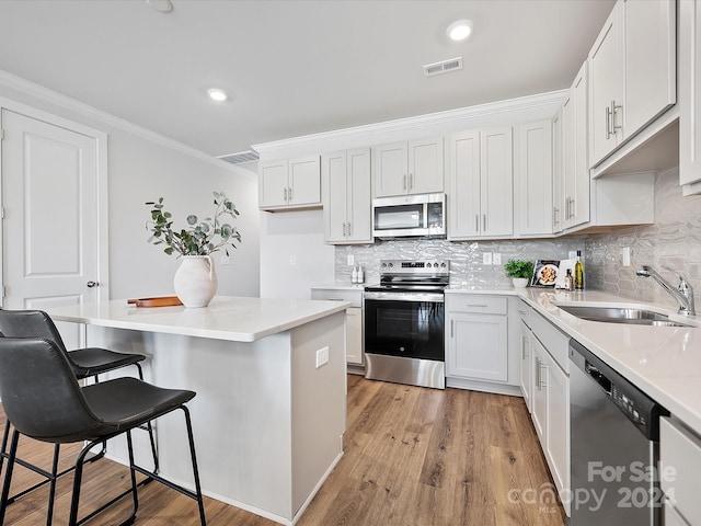 kitchen with white cabinets, sink, stainless steel appliances, light wood-type flooring, and a kitchen bar