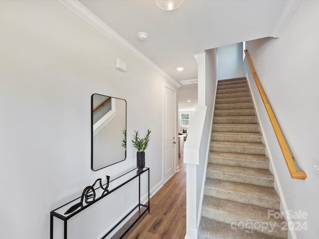 staircase with wood-type flooring and ornamental molding