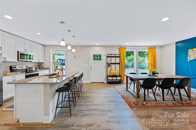 kitchen with light hardwood / wood-style flooring, sink, an island with sink, appliances with stainless steel finishes, and white cabinets