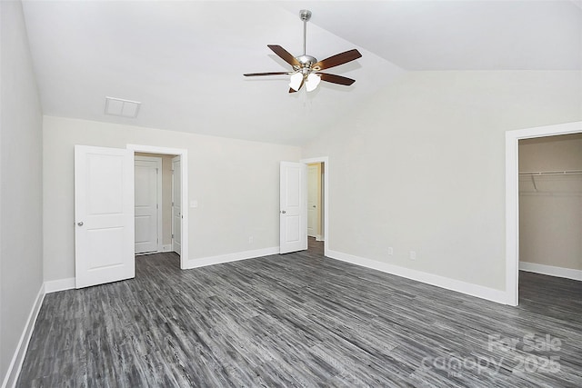unfurnished bedroom featuring lofted ceiling, dark wood-type flooring, baseboards, and a walk in closet