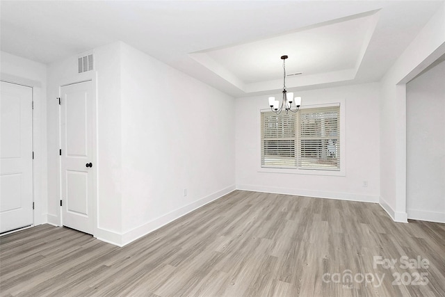 unfurnished room featuring light wood-type flooring, baseboards, a tray ceiling, and a chandelier