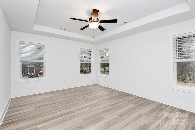 spare room with a tray ceiling, visible vents, and light wood-style floors